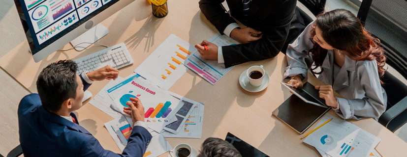 Visão superior de uma mesa com vários papéis de negócios, canetas, xícaras de café e em volta, várias pessoas sentadas
