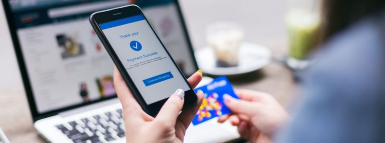 Imagem de uma mulher mexendo no celular em frente a um notebook