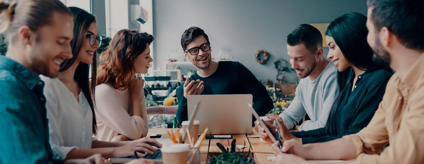 várias pessoas em volta de uma mesa de reuniões, mexendo em notebook e celulares