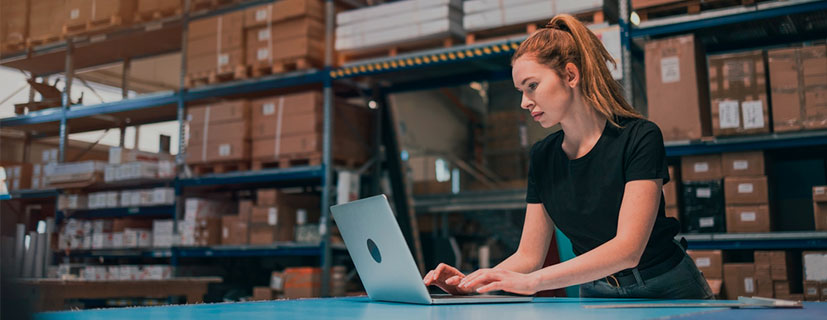 mulher digitando no notebook que está em cima de uma mesa dentro de um estoque