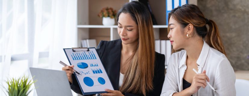 transformação digital: duas mulheres olhando o relatório na prancheta em frente ao notebook