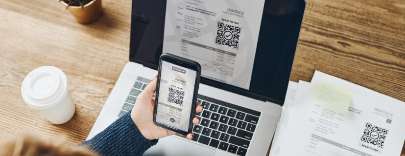 Mãos segurando o celular com a tela um qr code em frente ao computador