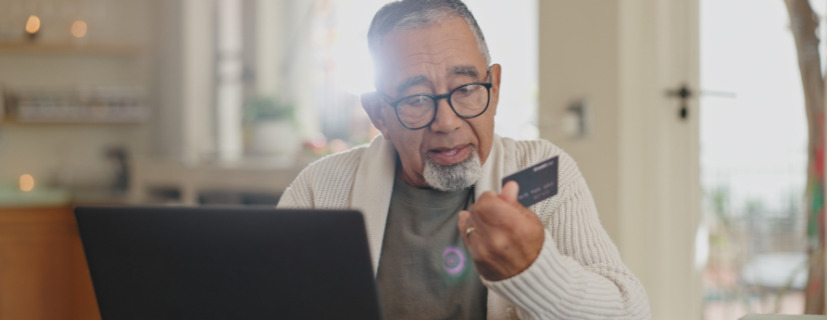 Homem utilizando um notebook com um cartão em mãos
