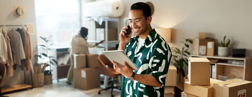 Homem falando ao celular e com um tablet em mãos.